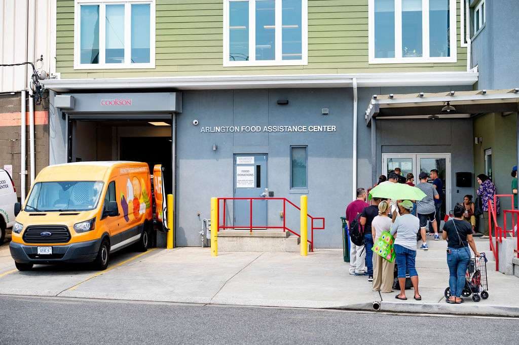 Outside of Arlington Food Assistance Center with a van parked outside of the garage on the left and a line of people on the right